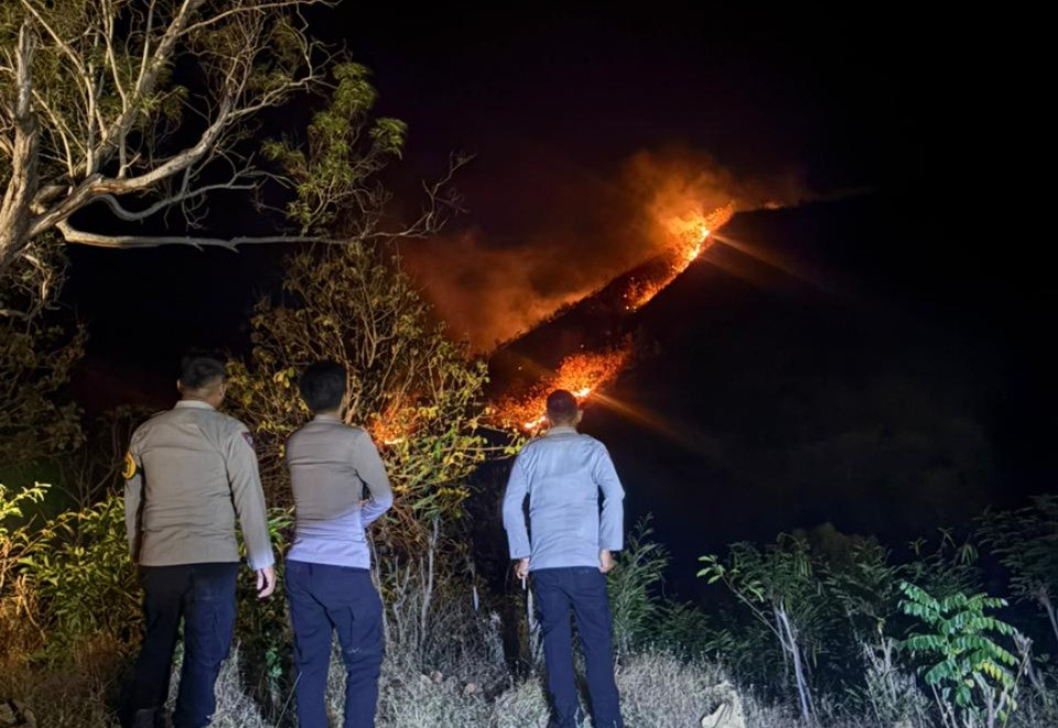 Ketgam: Personel Polsek Sendana memantau kobaran api yang melanda kawasan perbukitan Lembang, Majene, Senin (31/8/2026) malam. Api terus meluas akibat tiupan angin kencang dan medan yang sulit dijangkau.