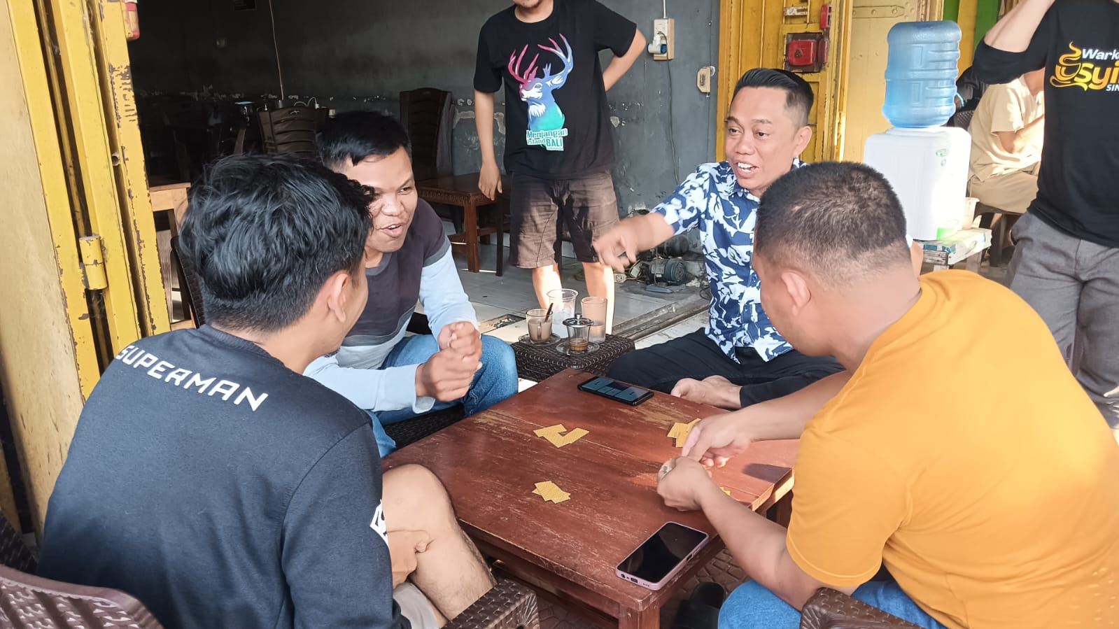 Sejumlah warga menikmati permainan domino bersama di sebuah warung. Selain menjadi hiburan dan ajang mempererat silaturahmi, permainan domino juga menjadi ruang menguji ketenangan, strategi, sportivitas, dan kejujuran para pemain.